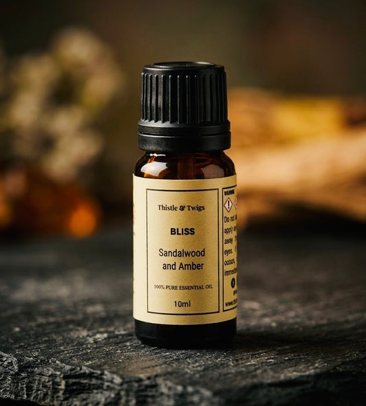 Thistle & Twigs Bliss Sandalwood and Amber essential oil, 10ml amber bottle with a pale yellow label and black cap, displayed on a rustic dark surface.