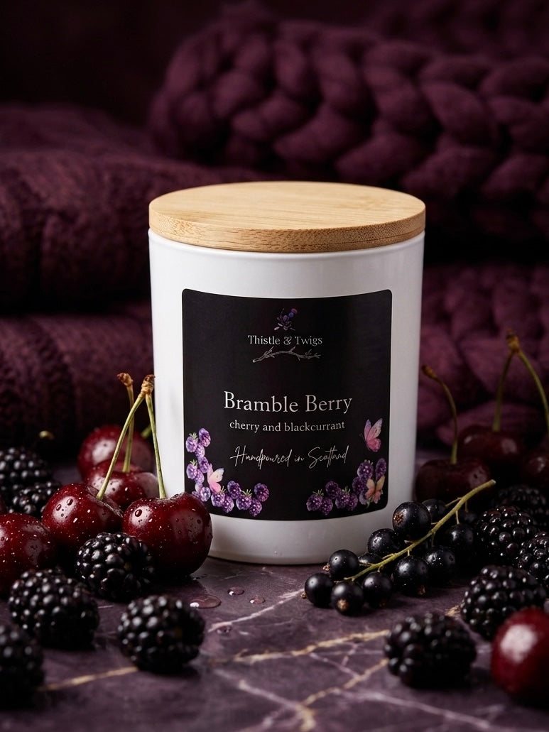 Thistle & Twigs Bramble Berry cherry and blackcurrant soy wax candle with bamboo lid, surrounded by fresh cherries, blackberries and blackcurrants on a dark purple marble surface