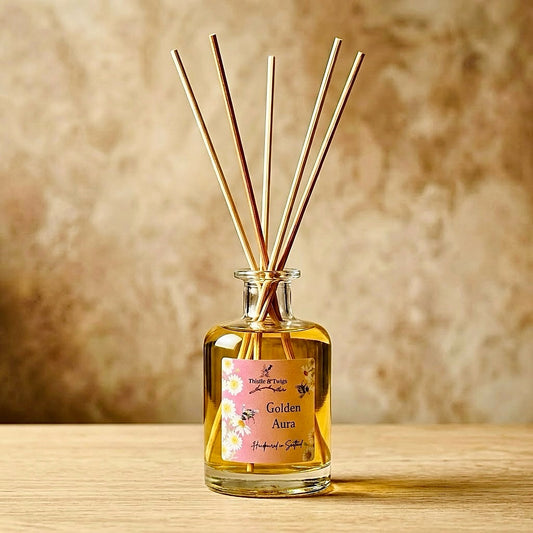 Thistle & Twigs Golden Aura reed diffuser with natural reeds and a floral bee label, on a light wooden surface against a beige background