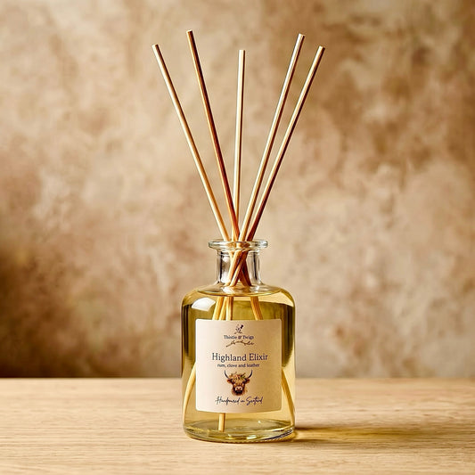 Thistle & Twigs Highland Elixir reed diffuser with natural reeds and a Highland cow label, on a light wooden surface against a beige background