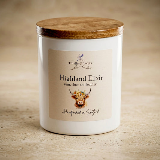 Thistle & Twigs Highland Elixir rum, clove and leather soy wax candle with wooden lid and Highland cow illustration label, hand poured in Scotland