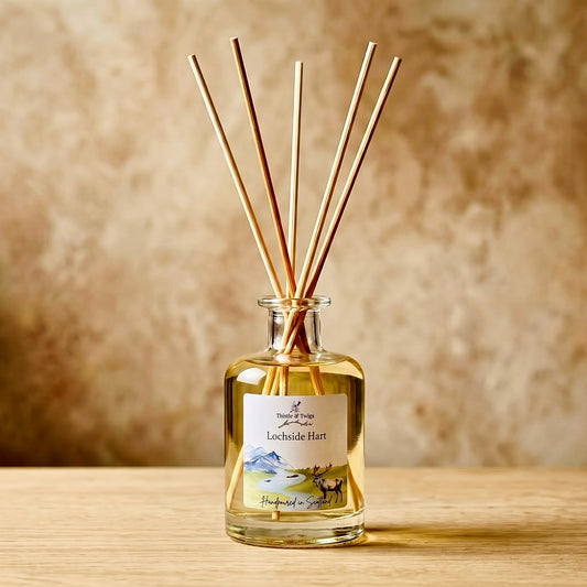 Thistle & Twigs Lochside Hart reed diffuser with natural reeds and a stag and mountain landscape label, on a light wooden surface against a beige background.
