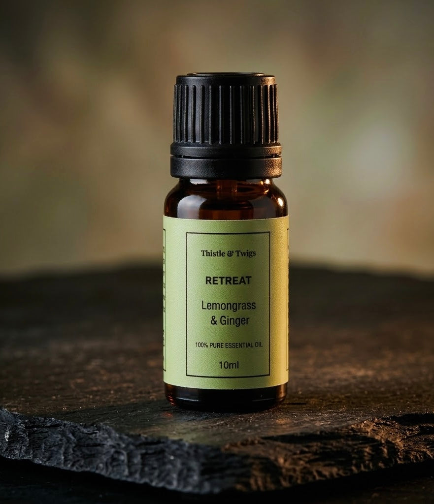 Thistle & Twigs Retreat Lemongrass & Ginger essential oil, 10ml amber bottle with a pale green label and black cap, displayed on a rustic wooden surface