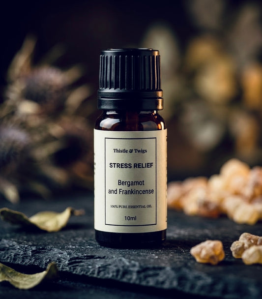 Thistle & Twigs Stress Relief Bergamot and Frankincense essential oil, 10ml amber bottle with a cream label and black cap, displayed on dark slate beside resin pieces and dried leaves.