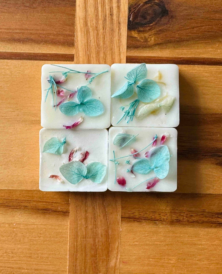 Close-up of four Thistle & Twigs Tonka Botanical Soy Wax Melts showing pressed blue hydrangea petals, pink rosebuds and delicate botanical stems embedded in white soy wax