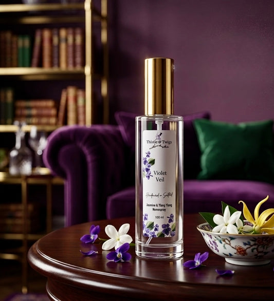Thistle & Twigs Violet Veil 100ml home spray on a mahogany table in a luxurious purple interior with violet, jasmine and ylang ylang flowers