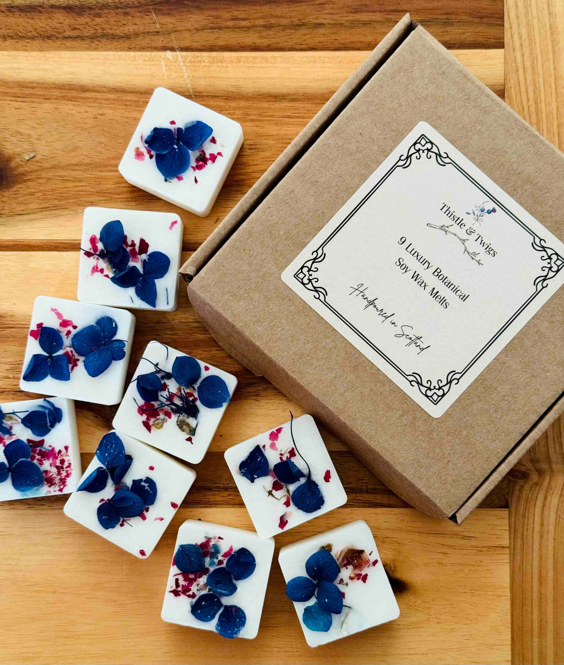 wood-spices-leather-botanical-soy-wax-melt. Decorative soy wax melts with floral designs on a wooden surface next to a cardboard box.